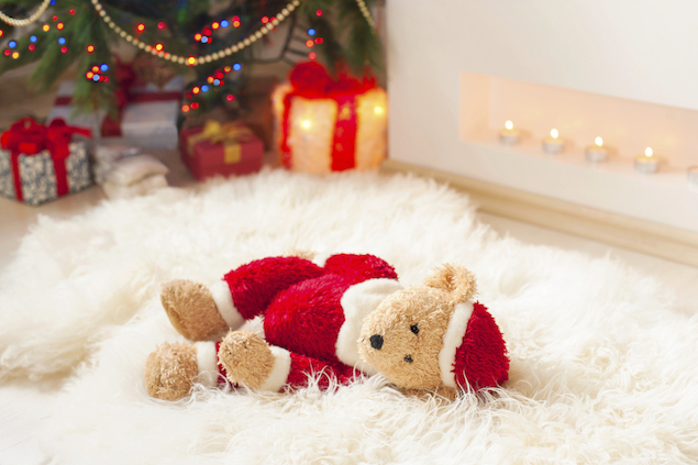 Santa teddy bear toy on sheepskin near illuminated christmas tree