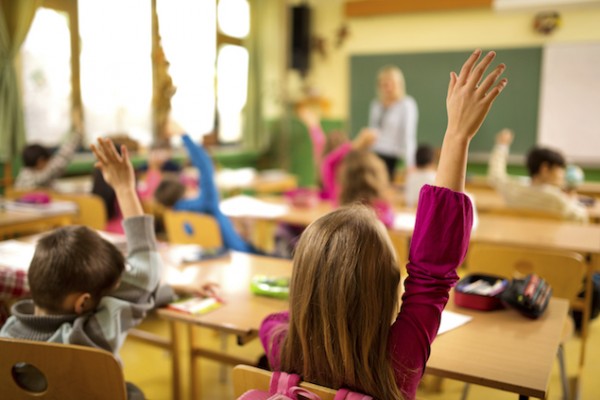 Children with hands raised in class at school