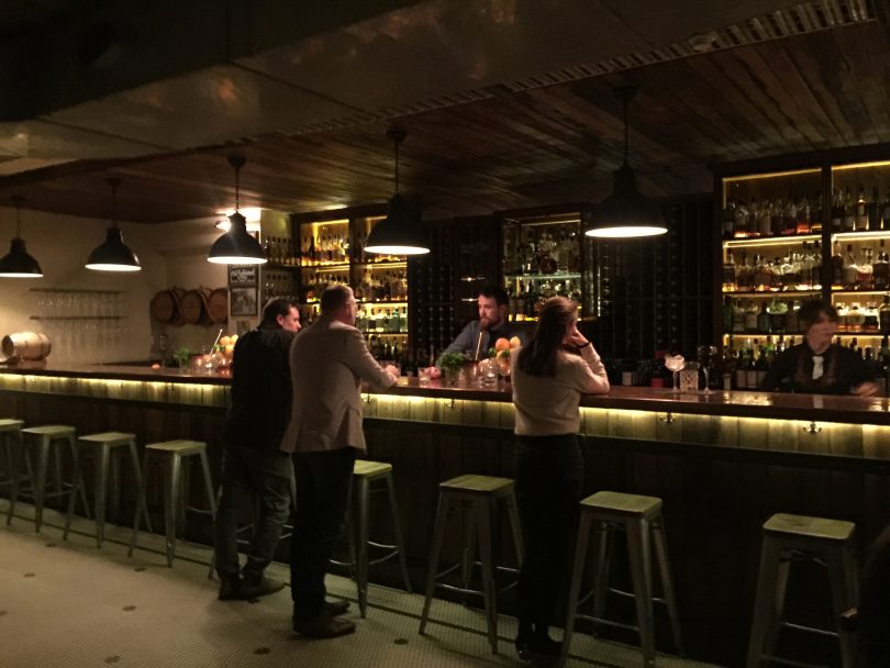 Two men and a woman standing at a bar, talking to a bartender.