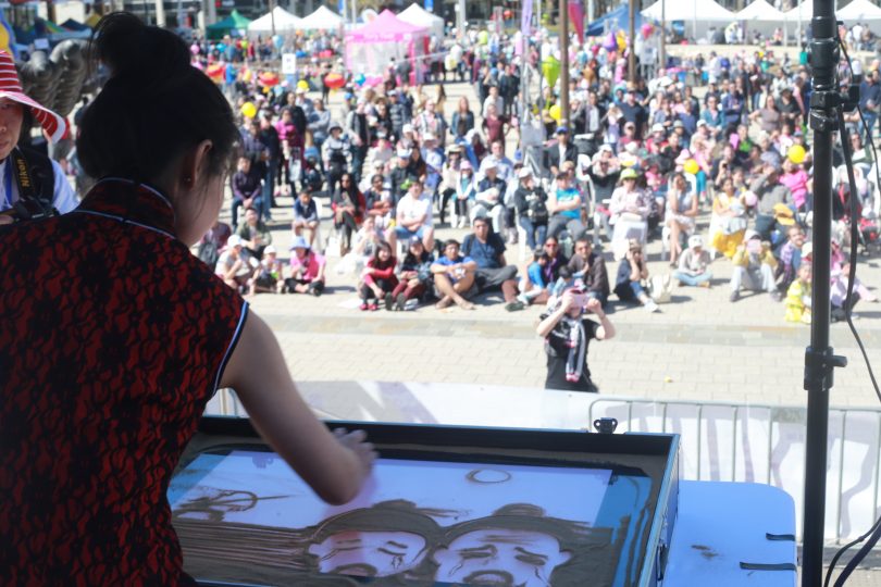 woman drawing sand art on stage in front of crowd