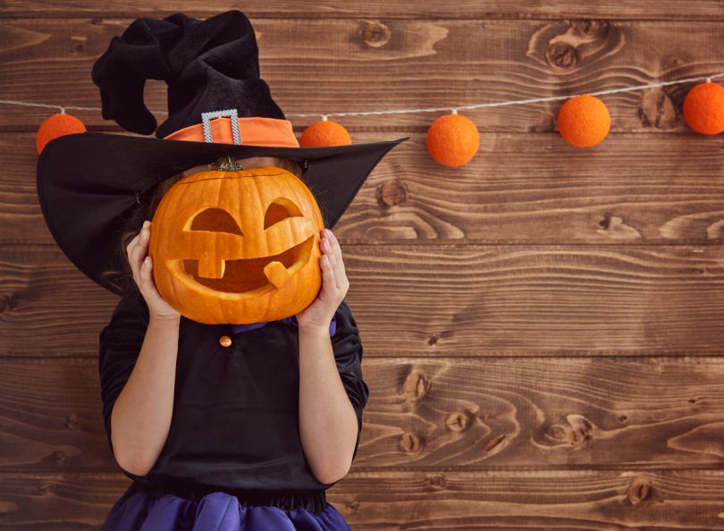 child holing a pumpkin in front of her face