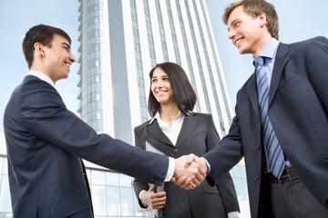 Two businessmen shaking hands with woman looking on