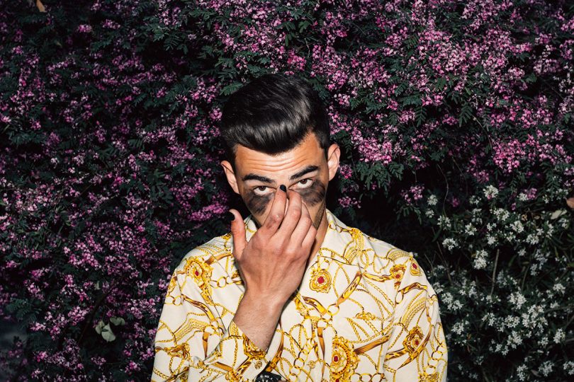 Kirlandd adjusting his sunglasses in front of floral backdrop.