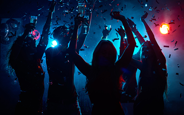 People dancing in a nightclub while holding drinks and confetti falling all around him.