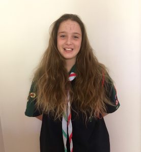 Girl in Scout uniform with long brown hair smiling at the camera