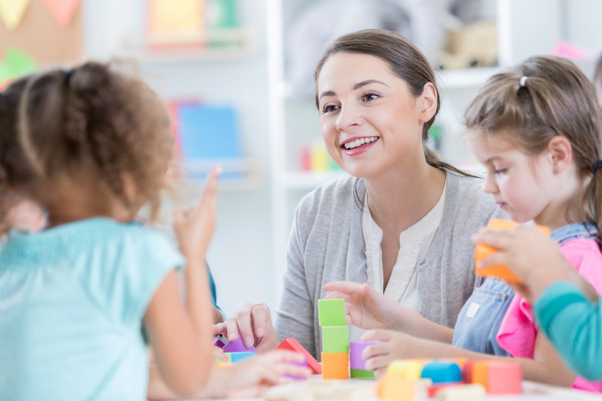 Childcare career - woman talks with two children a play table.