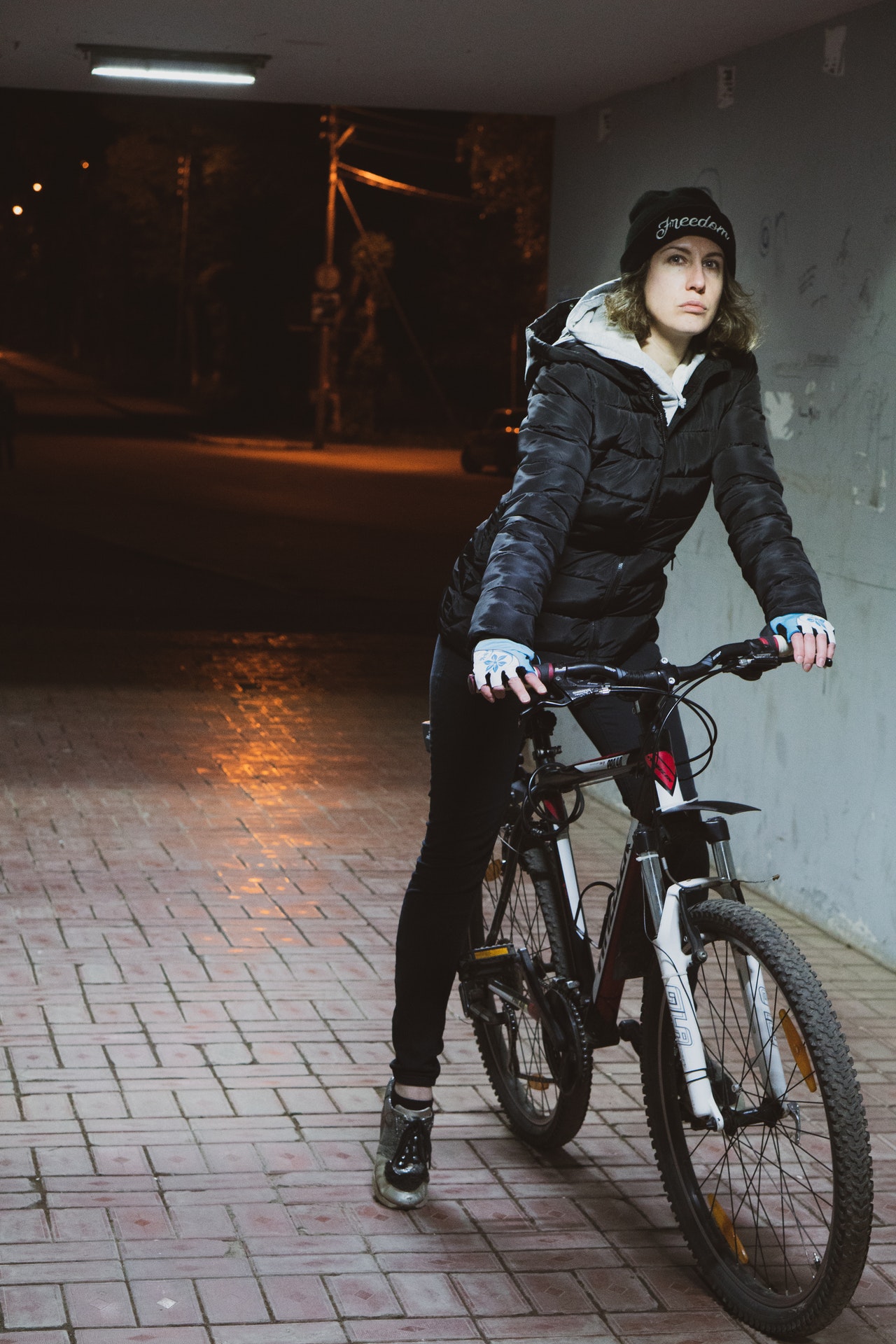 Woman on bicycle at night wearing a parka and beanie, riding a bicycle