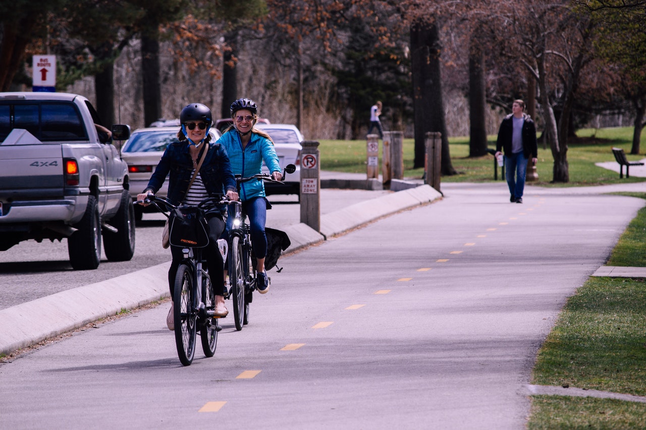 Two women riding bicycles on a cycle path separated from the road and cars