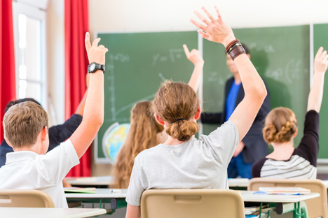 School children with hands raised in class.