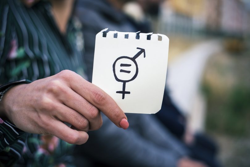 closeup of a young woman outdoors showing a piece of paper in front of her with a symbol for gender equality drawn in it.