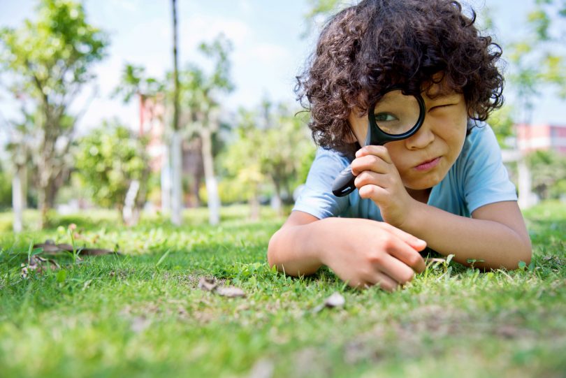 Little boy with magnifying glass in park.