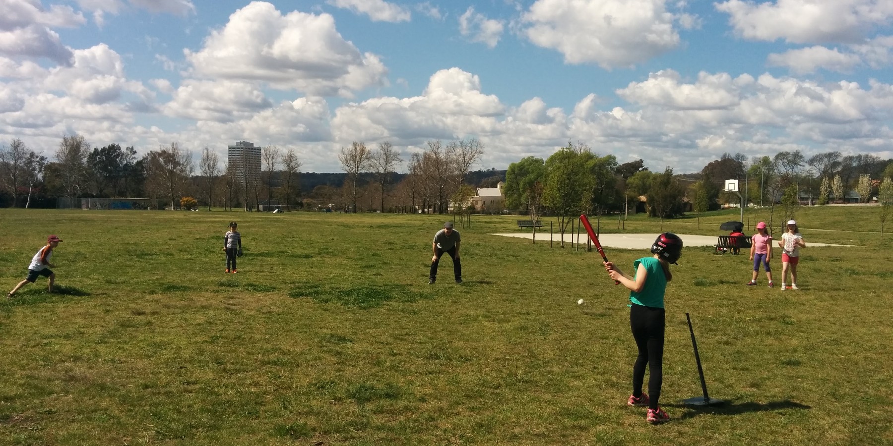 Kids and adults playing baseball in a park