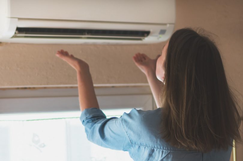 Women dying from the heat standing in front of the air conditioner.