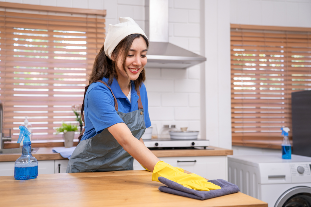 a woman wearing an apron and bandanna wiping down a kitchen bench