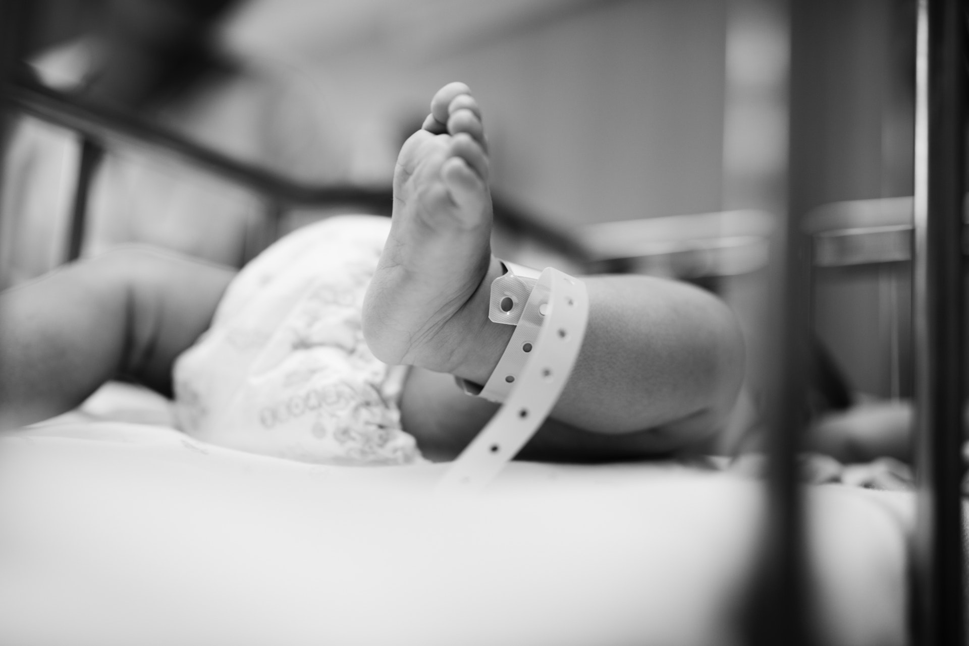 Black and white image of a newborn baby's foot with a hospital band on it, in a hospital crib