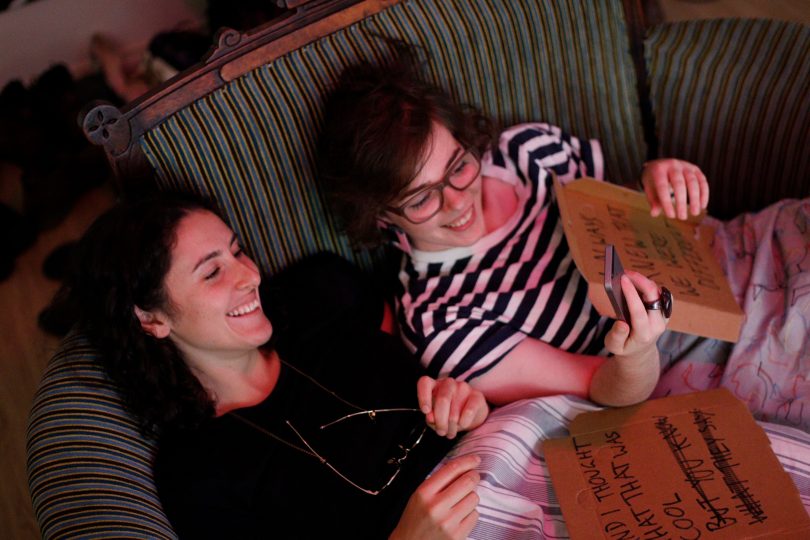 Photograph shows Heddy Blaazer and collaborator sitting on couch holding cardboard pieces