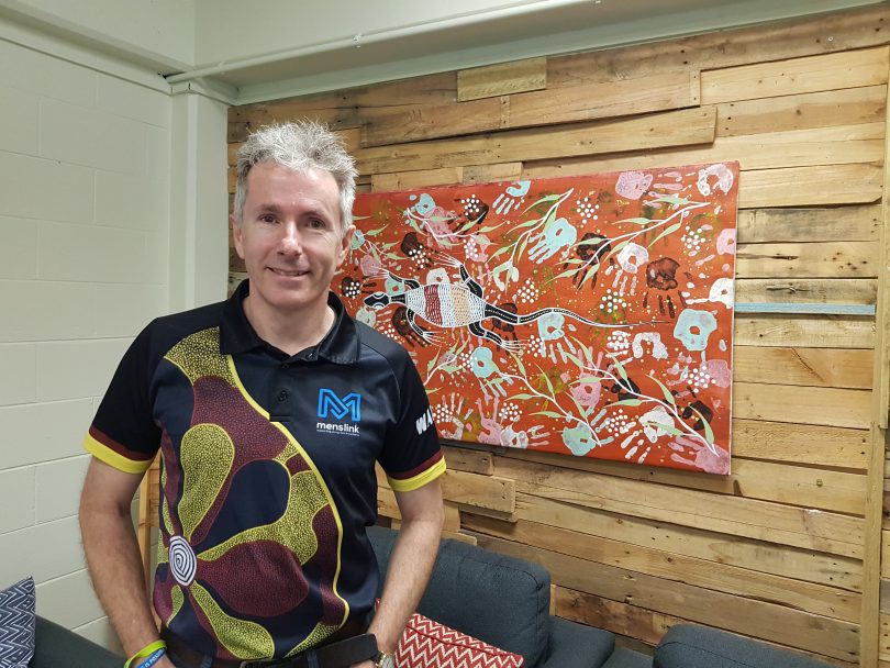 Martin Fisk from Menslink standing in front of Indigenous artwork.