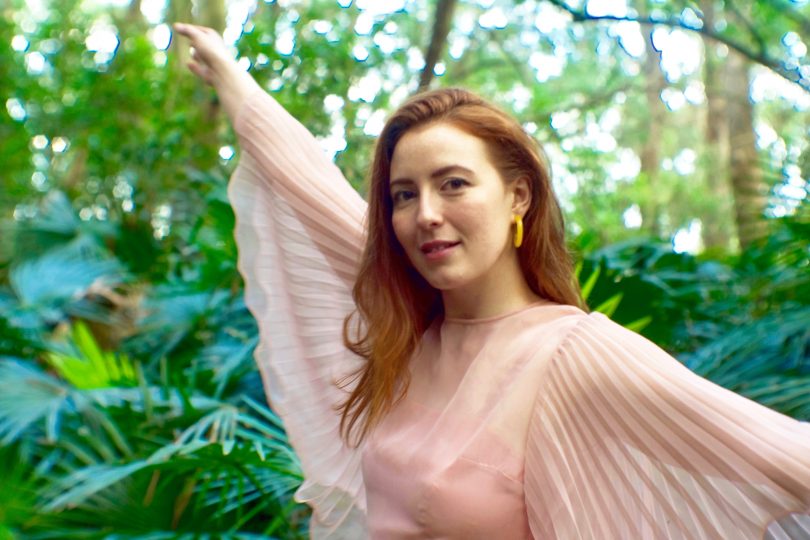 Female singer India Sweeney poses, arms outstretched, surrounded by rainforest