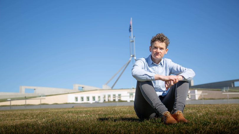 Dr Sophie Lewis sitting on grass in front of Parliament House.