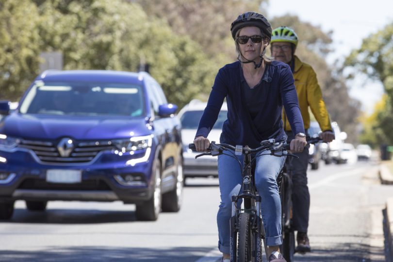 Woman and man riding bicycles in line of traffic in Canberra