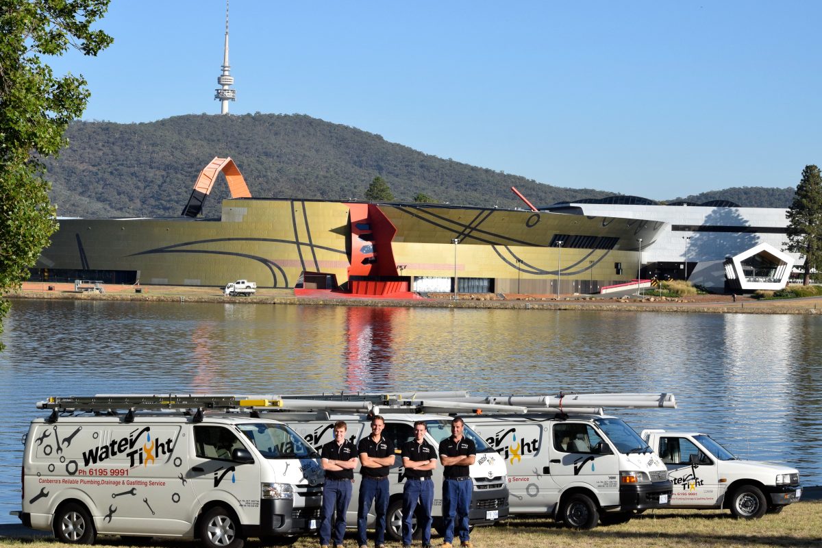 a group of 5 people wearing uniform standing in front of trucks at Lake Burley Griffin with the National Museum and Telstra Tower in the background