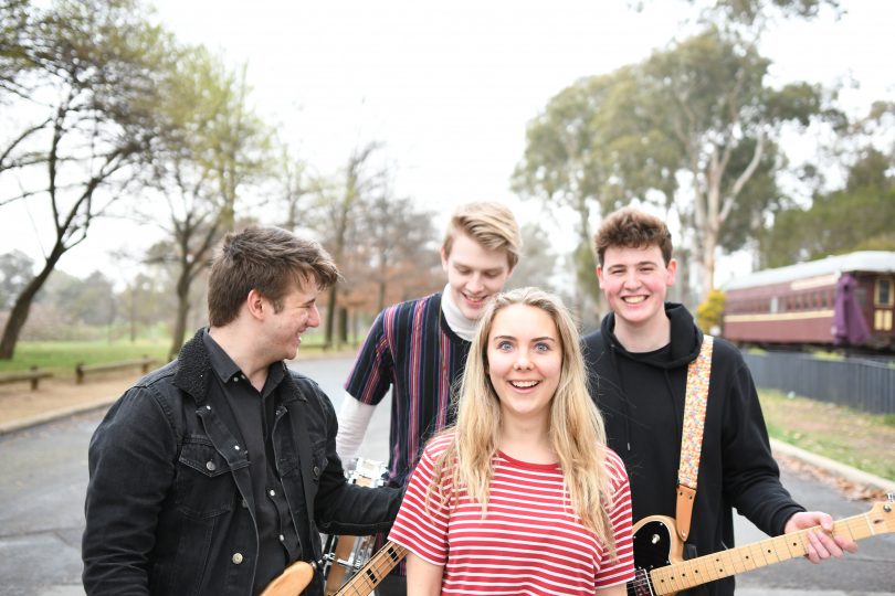 Photograph shows 4 band members on a suburban street with their instruments