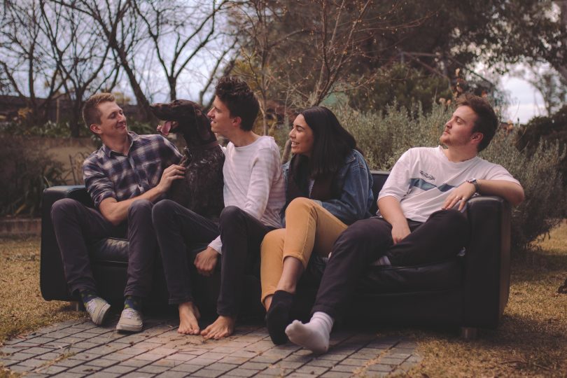 Photograph shows four members of ARCHIE sitting on outdoor couch