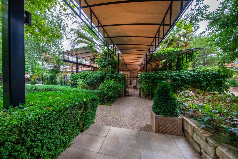 Evergreen shrubs and a covered walkway lead to the outdoor entertaining area