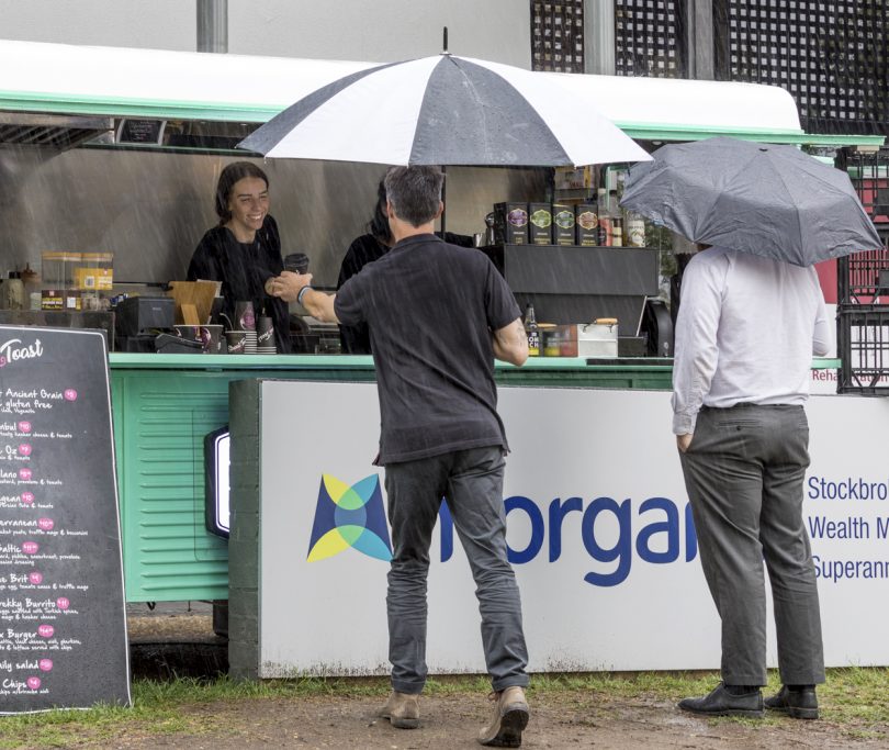 Customers with umbrellas at coffee cart.