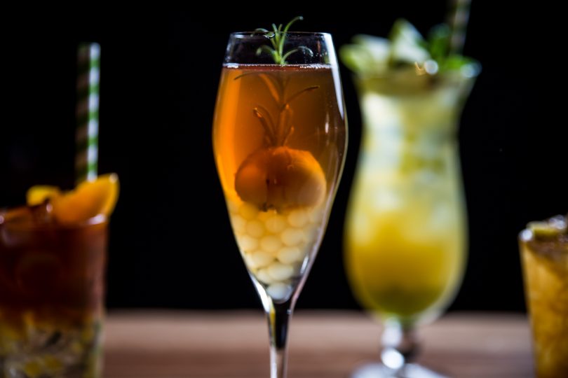 Close up of yellow cocktail, with three cocktails in background.