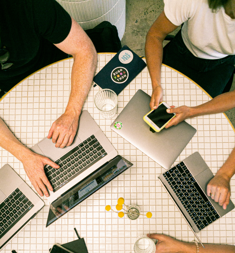 Three people sitting around a table with laptops and phones on the table.