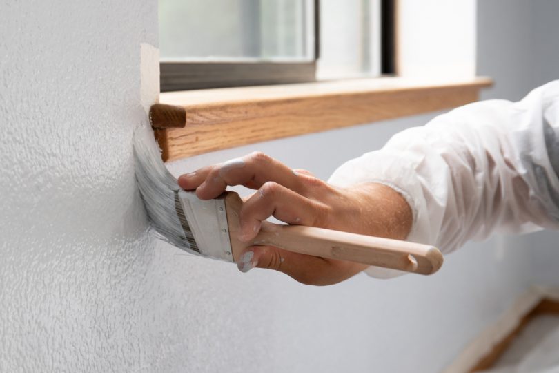 Close-up of person painting white wall.