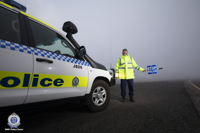 Police officer standing roadside with "stop police" sign.