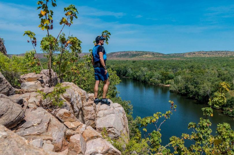 Hiker standing on cliff looking at view of river.