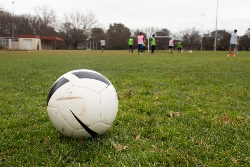 Soccer ball on grass, people playing in background.