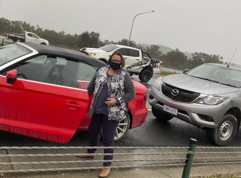 Anne Cahill Lambert standing next to stationary car in traffic at NSW/Victoria border.