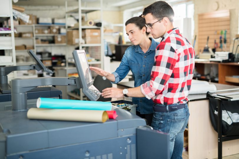 two people looking at a touchscreen on a large printer