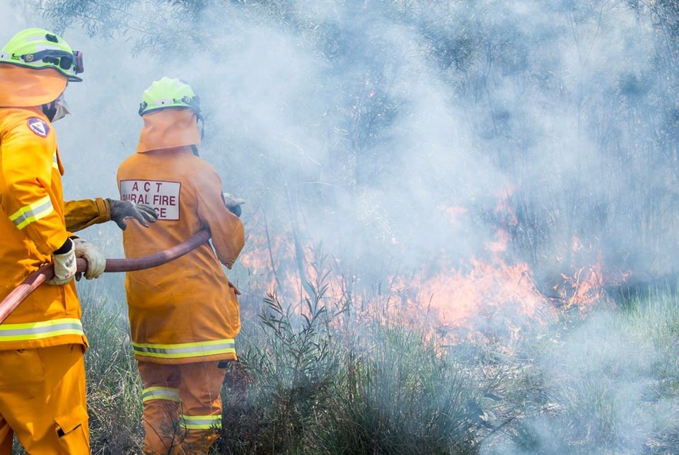 Firefighters from ACT Rural Fire Service holding hose in front of bushfire.