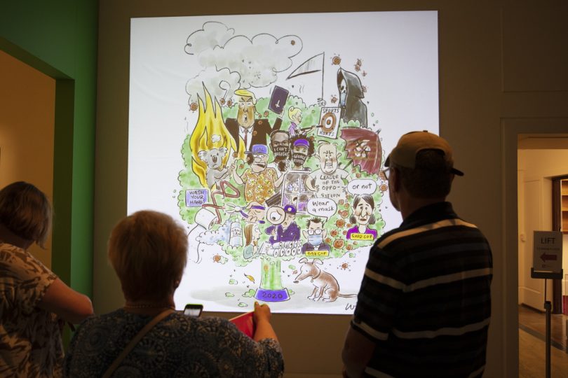 Three people viewing cartoon in Behind the Lines exhibition.