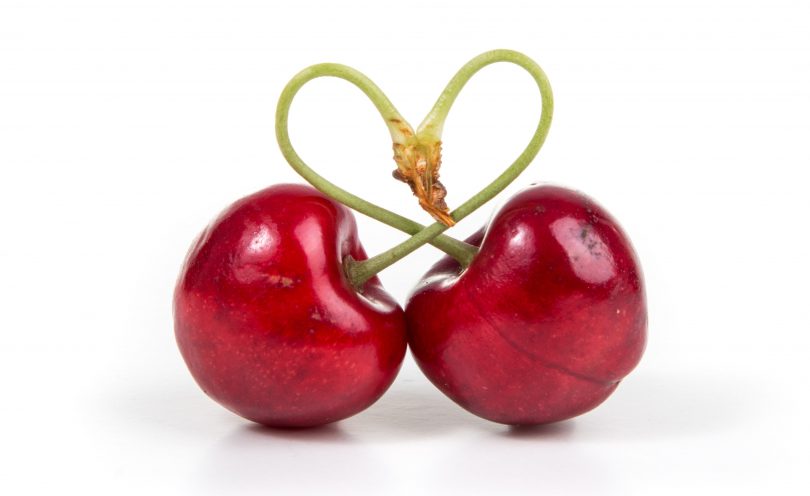 Two cherries tied together with stems forming love heart.