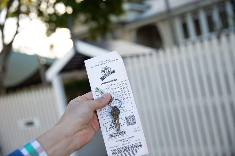 Person holding house keys and winning lotto ticket.