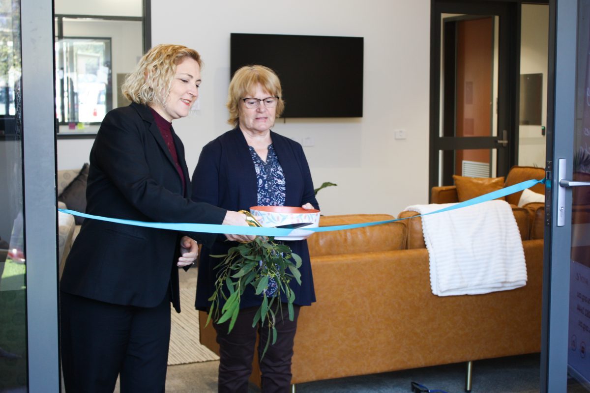 woman cuts ribbon next to a woman holding a bowl of water