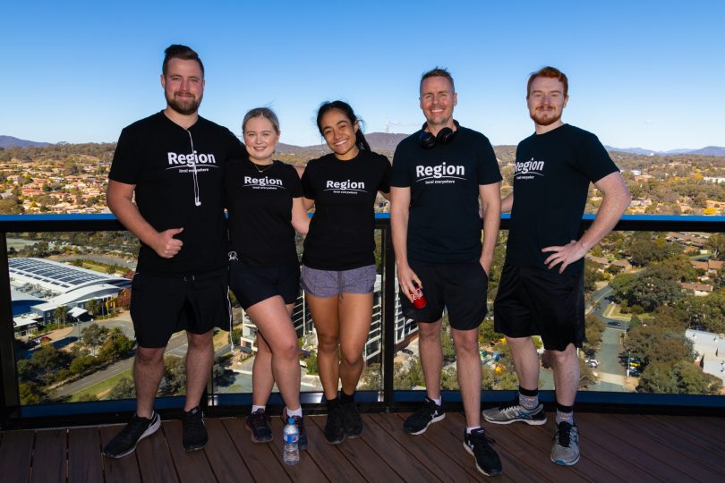 Five people standing on the top of a high building with blue sky behind them