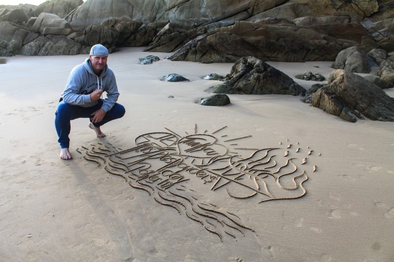 man crouching on beach next to sand writing