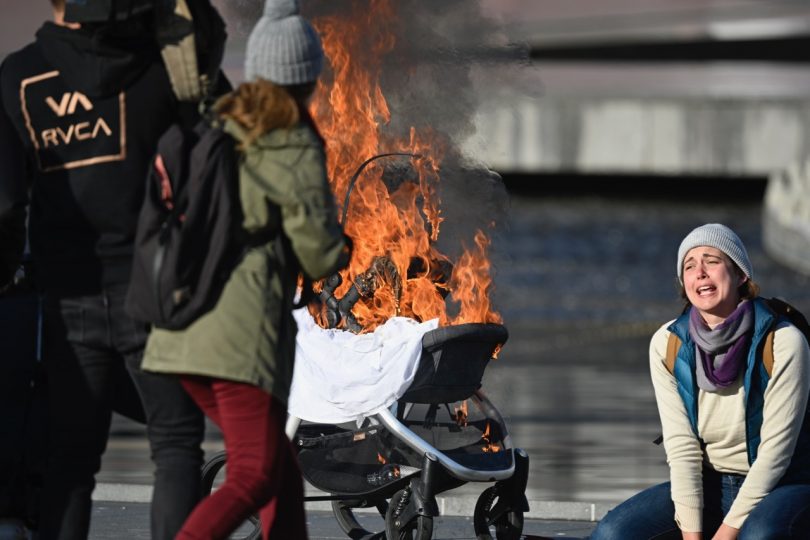 A woman kneels next to a burning pram