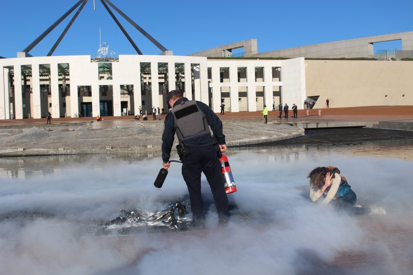 Man extinguishing burning pram outside Parliament House with protestor on ground