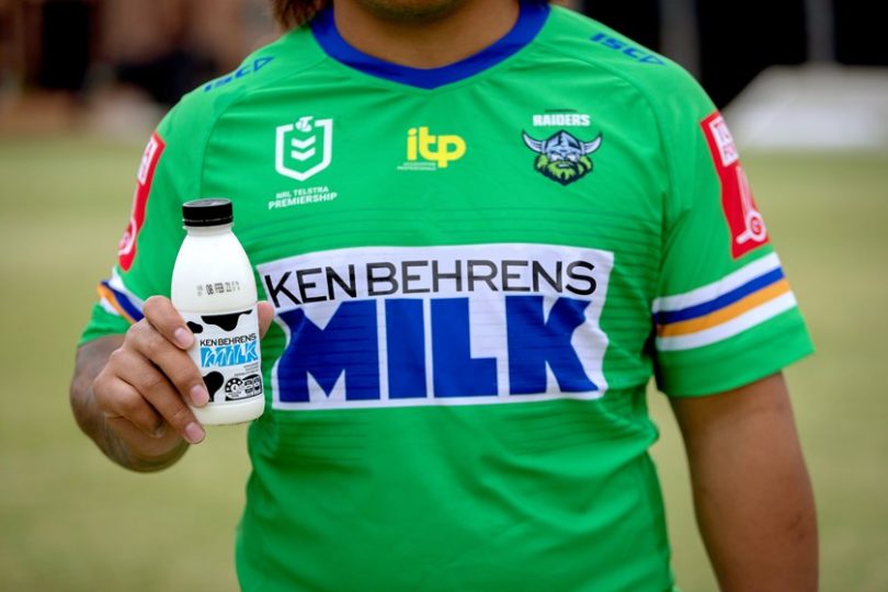 Man wearing Canberra Raiders 'Ken Behrens' jersey holding bottle of milk