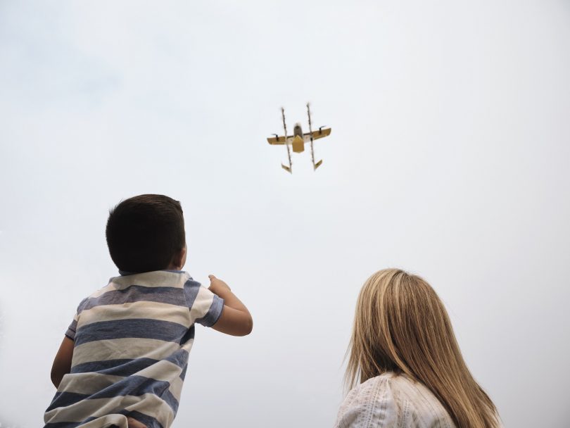 A Wing delivery drone over two people