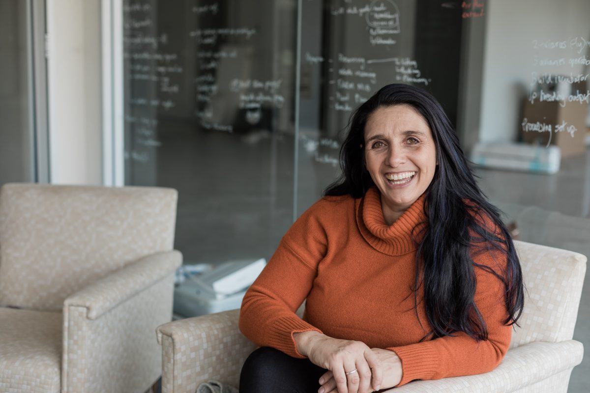 Woman with long black hair in orange jumper smiles at the camera.