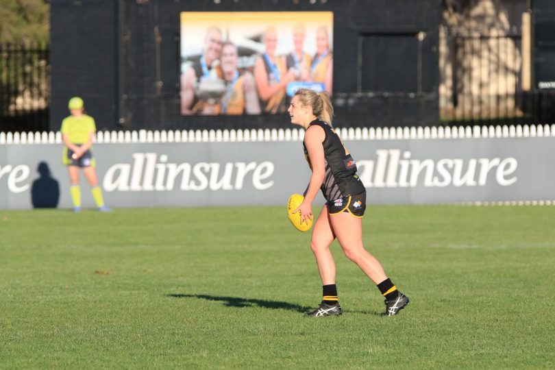 Woman playing Australian rules football with allinsure sign in background